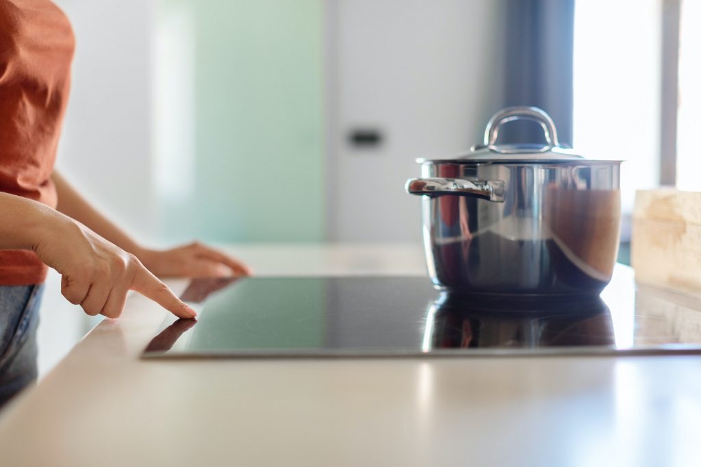 Female hand turning on induction stove with steel cooking pan in kitchen